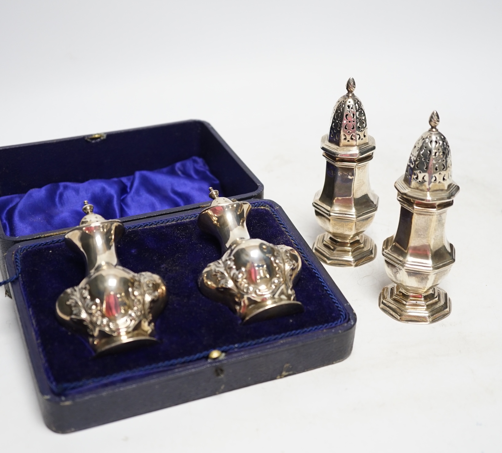 A cased pair of George V silver pepperettes, by Joseph Gloster Ltd, Birmingham, 1912, 98mm and a pair of Edwardian silver octagonal pepperettes, 6.3oz. Fair condition.